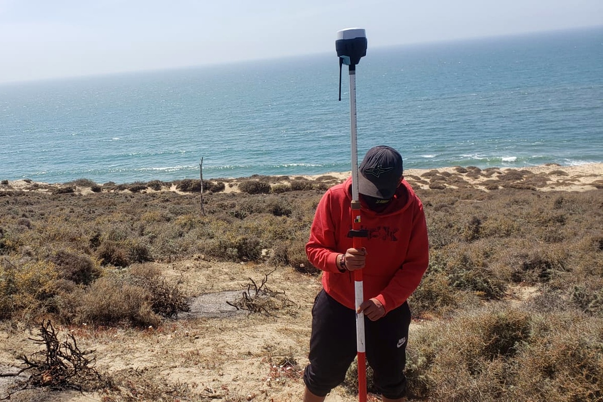 Topógrafo tomando datos con bastón GNSS en acantilado costero